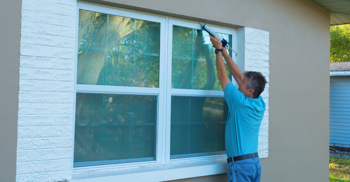 Man weatherproofing windows for winter