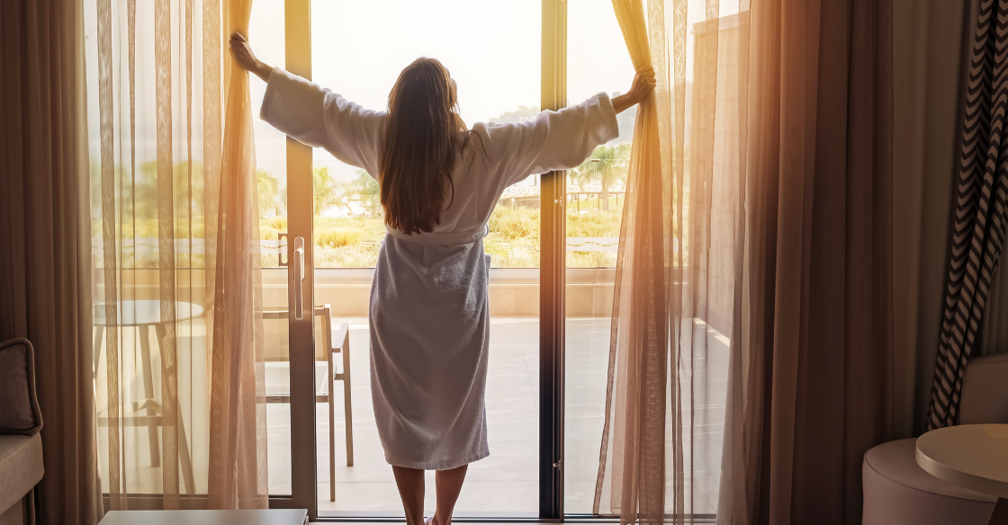 Room standing in front of her hotel room's sliding glass doors